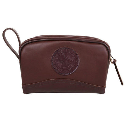 A brown smooth Duluth Pack Leather Sportsman's Kit Bag with a circular logo and zipper pull, shown from the front against a white background.