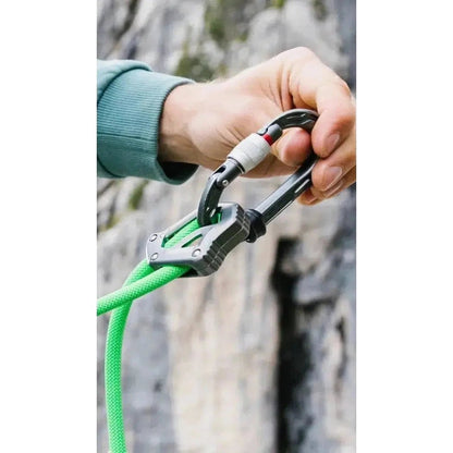 A hand attaches the Edelrid Switch Adjust 100cm carabiner to a Neon Green climbing rope against a rocky background.