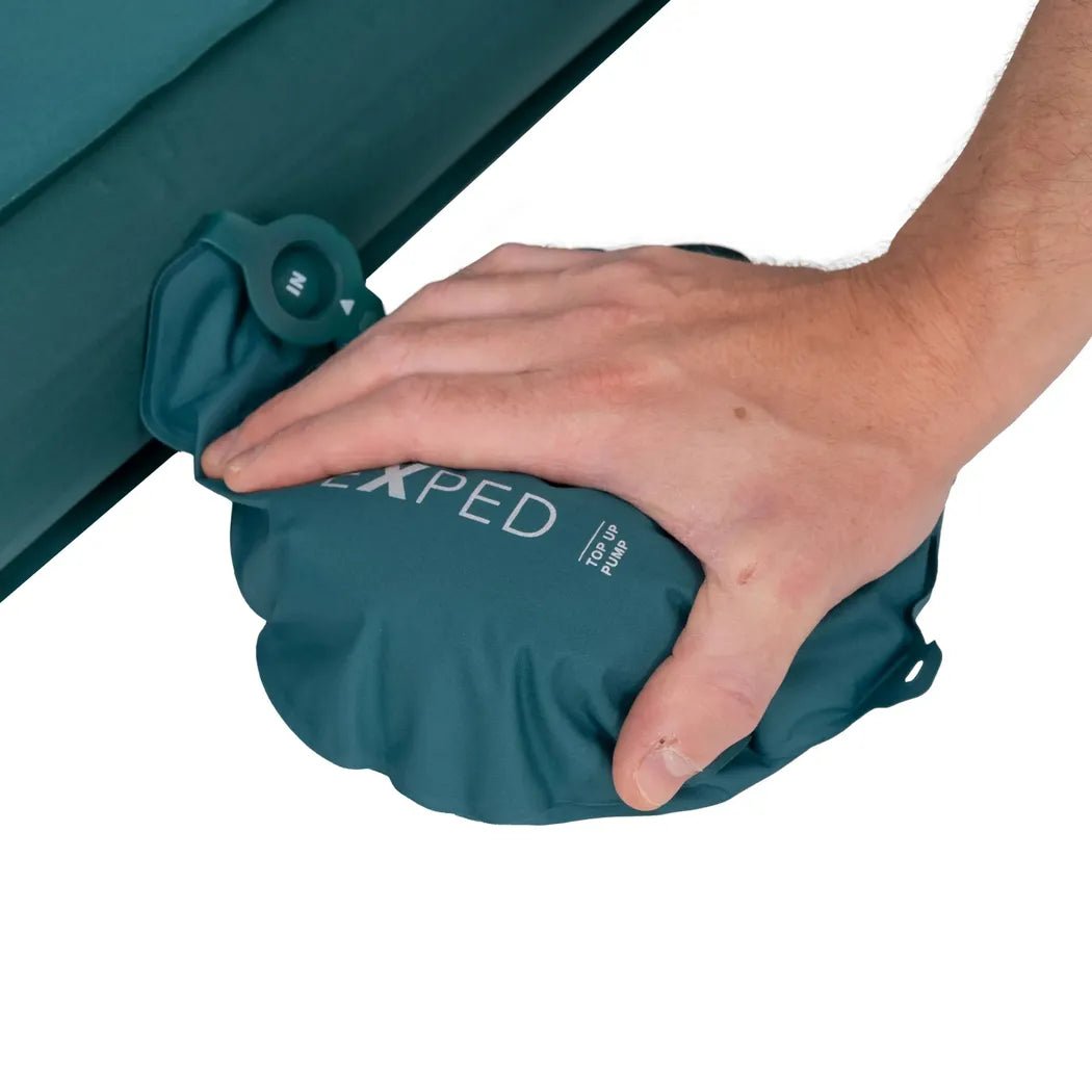 A hand presses the Exped MegaMat Duo sleeping pad against a teal-colored camping mat.