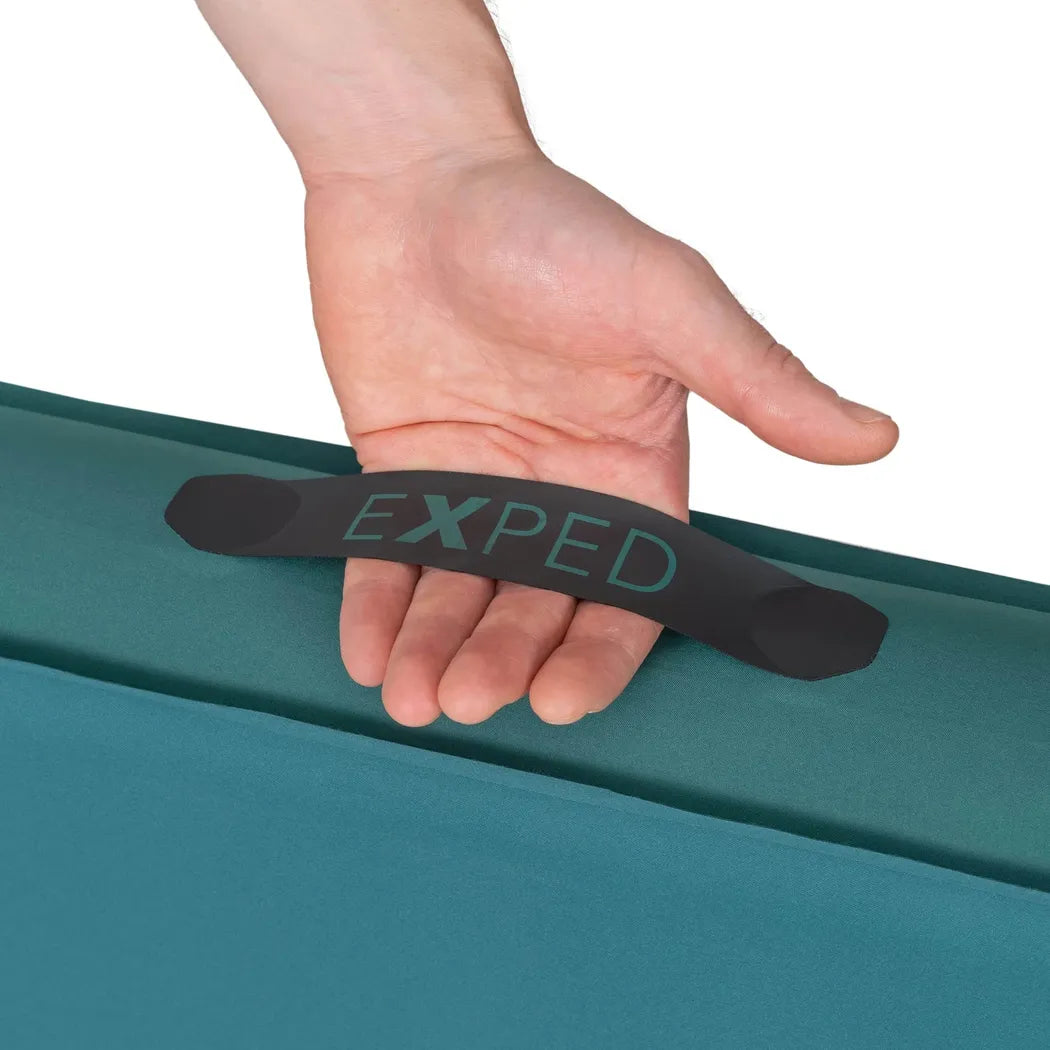 A hand holds the black handle of the teal Exped MegaMat against a white background.