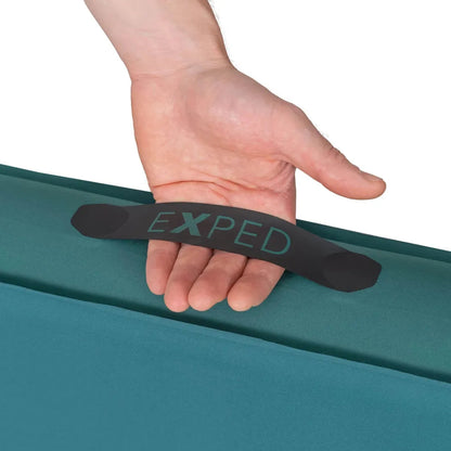 A hand holds the black handle of the teal Exped MegaMat against a white background.