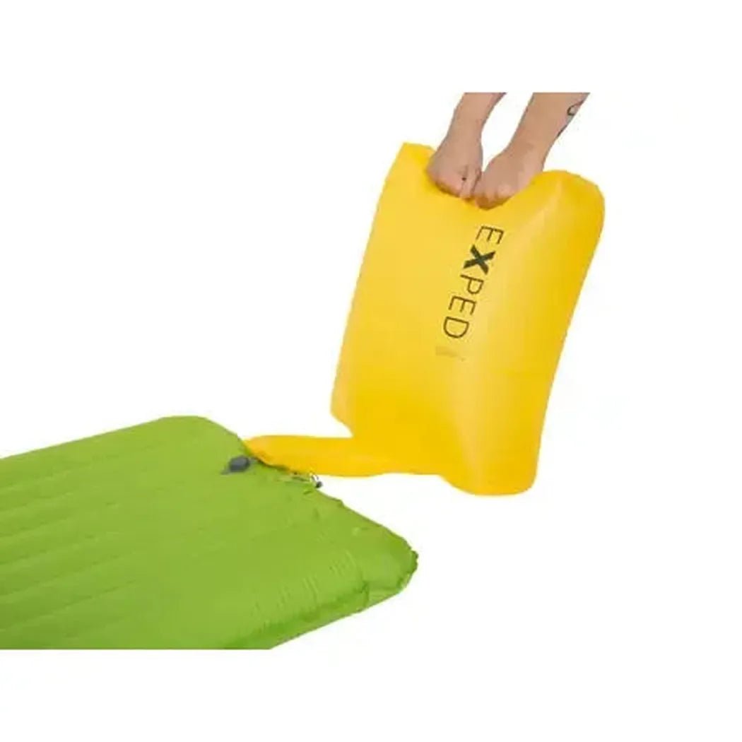 A person inflates the yellow Exped Ultra 6.5R sleeping pad next to a green one on a white background.
