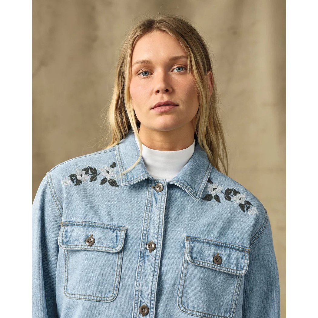 A front view of the Filson Womens Denim Shirt in Pale Indigo with embroidered shoulders, two chest pockets, and a white turtleneck underneath, against a neutral background.