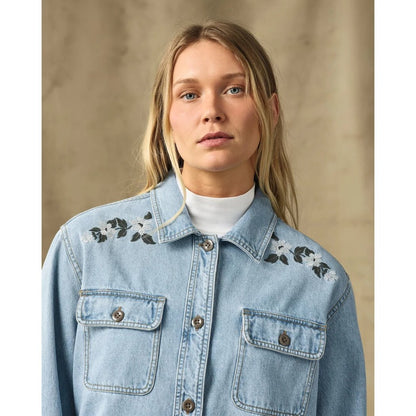 A front view of the Filson Womens Denim Shirt in Pale Indigo with embroidered shoulders, two chest pockets, and a white turtleneck underneath, against a neutral background.