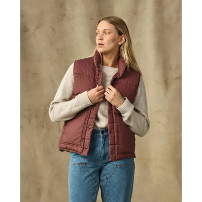 A woman wearing the Filson Womens Hertage Cotton Down Vest in SmokedPaprika stands against a neutral background.