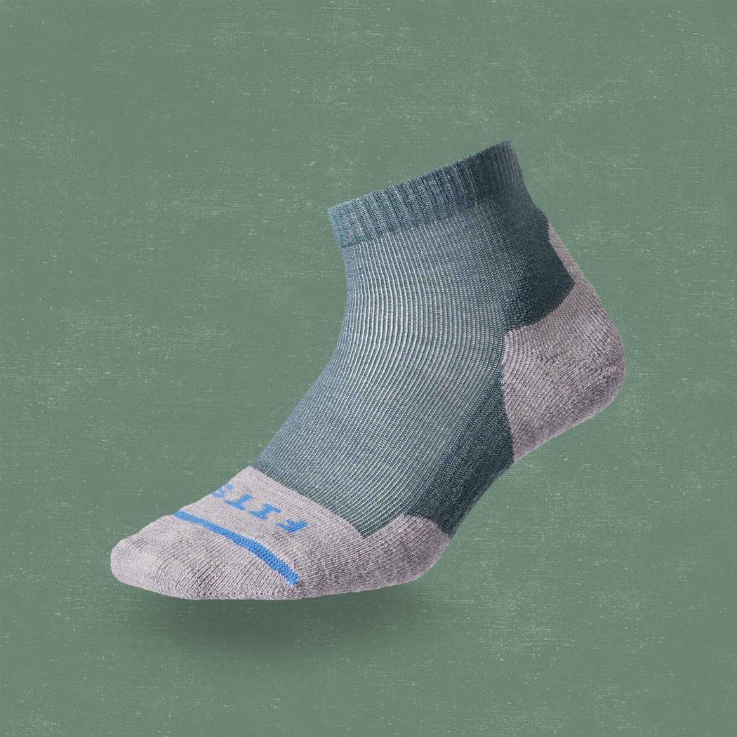 A side view of the FITS Light Hiker Quarter sock in Coal color on a green background.
