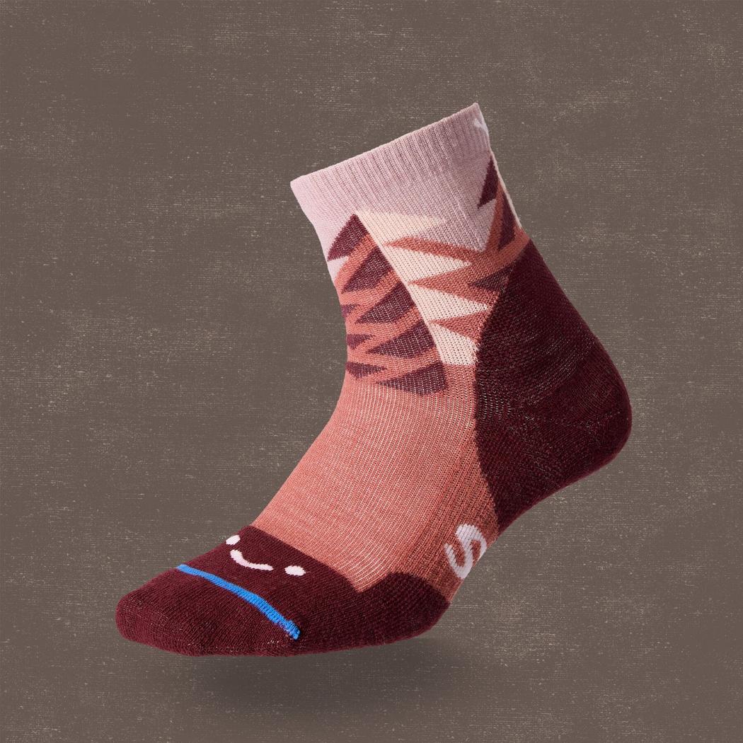 A side view of the FITS Light Quarter - Stand Fir socks in Marsala showing the smiley face toe and mountain pattern against a dark background.
