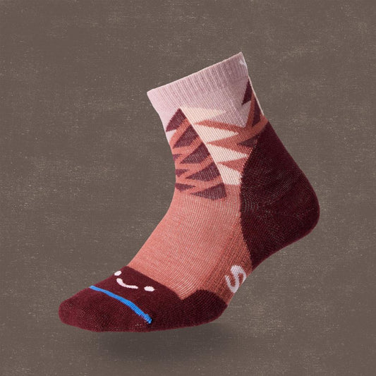 A side view of the FITS Light Quarter - Stand Fir socks in Marsala showing the smiley face toe and mountain pattern against a dark background.