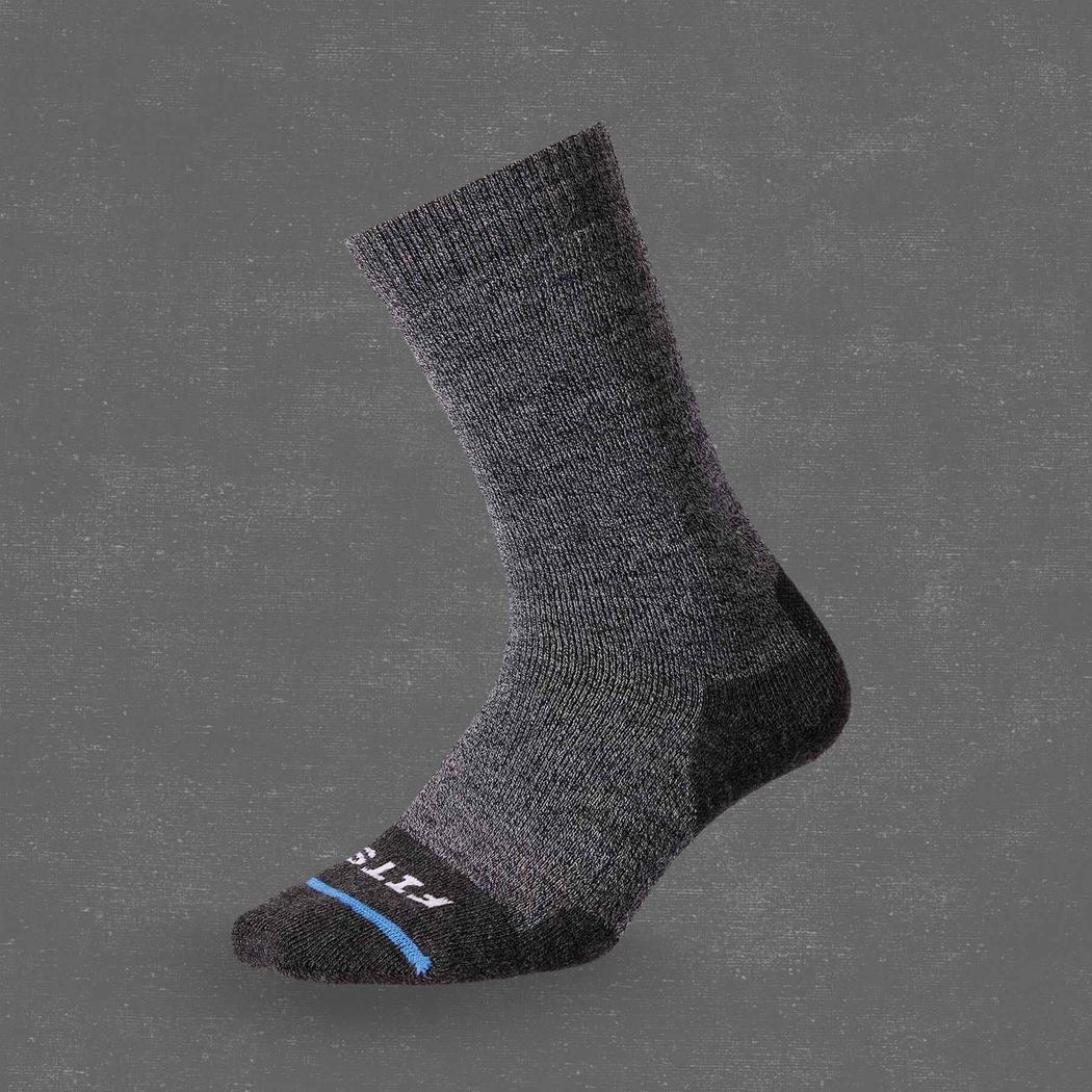 Side view of the FITS Medium Hiker Crew sock in Coal color with a black toe and heel against a gray background.