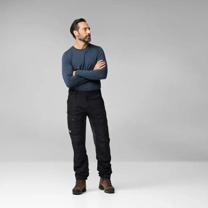 A man stands with crossed arms wearing the Fjallraven Men's Vidda Pro Ventilated Trs in Dark Grey-Black against a plain light background.