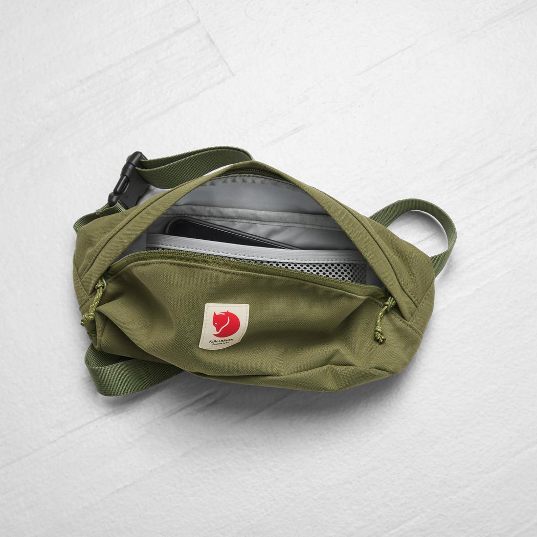 A top-down view of the Fjallraven Ulvo Hip Pack Medium in Black, showing its open main compartment with a phone inside, against a light gray background.