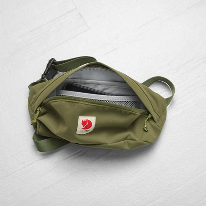A top-down view of the Fjallraven Ulvo Hip Pack Medium in Black, showing its open main compartment with a phone inside, against a light gray background.