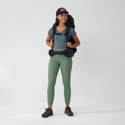 A front view of the Fjallraven Women's Abisko Tights in Patina Green worn by a model with a backpack against a plain white background.