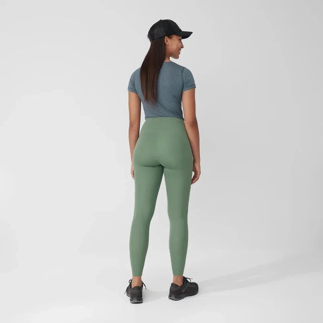 Back view of the Fjallraven Women's Abisko Tights in Patina Green on a model wearing a blue tee and black cap against a white background.