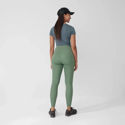 Back view of the Fjallraven Women's Abisko Tights in Patina Green on a model wearing a blue tee and black cap against a white background.