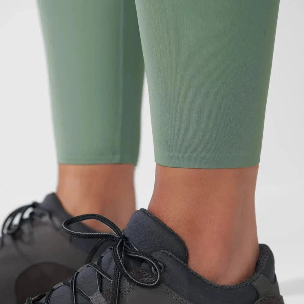 Side view of the Fjallraven Women's Abisko Tights in Patina Green on a model wearing charcoal sneakers against a white background.