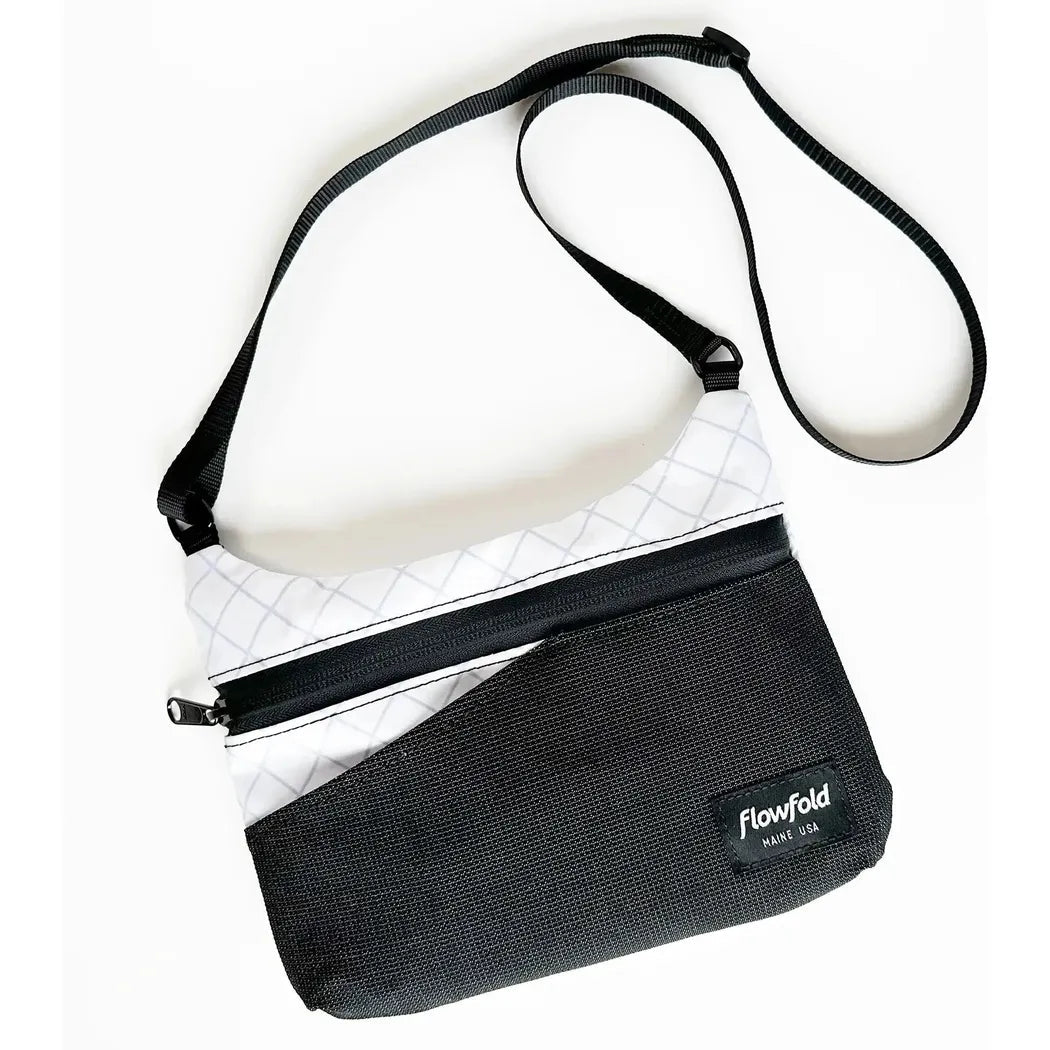 A top-down view of the Flowfold Eclipse Crossbody bag in Jet Black with a white upper section and black strap against a white background.