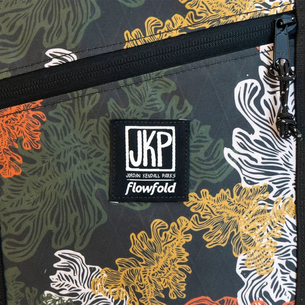 A close-up of the JKP Flowfold tote bag shows the brand patch and zipper against a dark, patterned background.