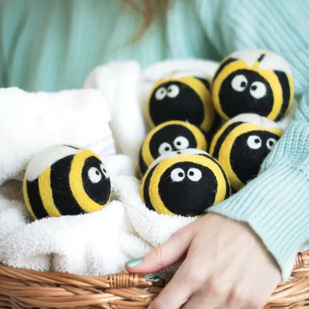 A hand holds a basket of Friendsheep Bee Trio Eco Wool Dryer Balls on a white towel.