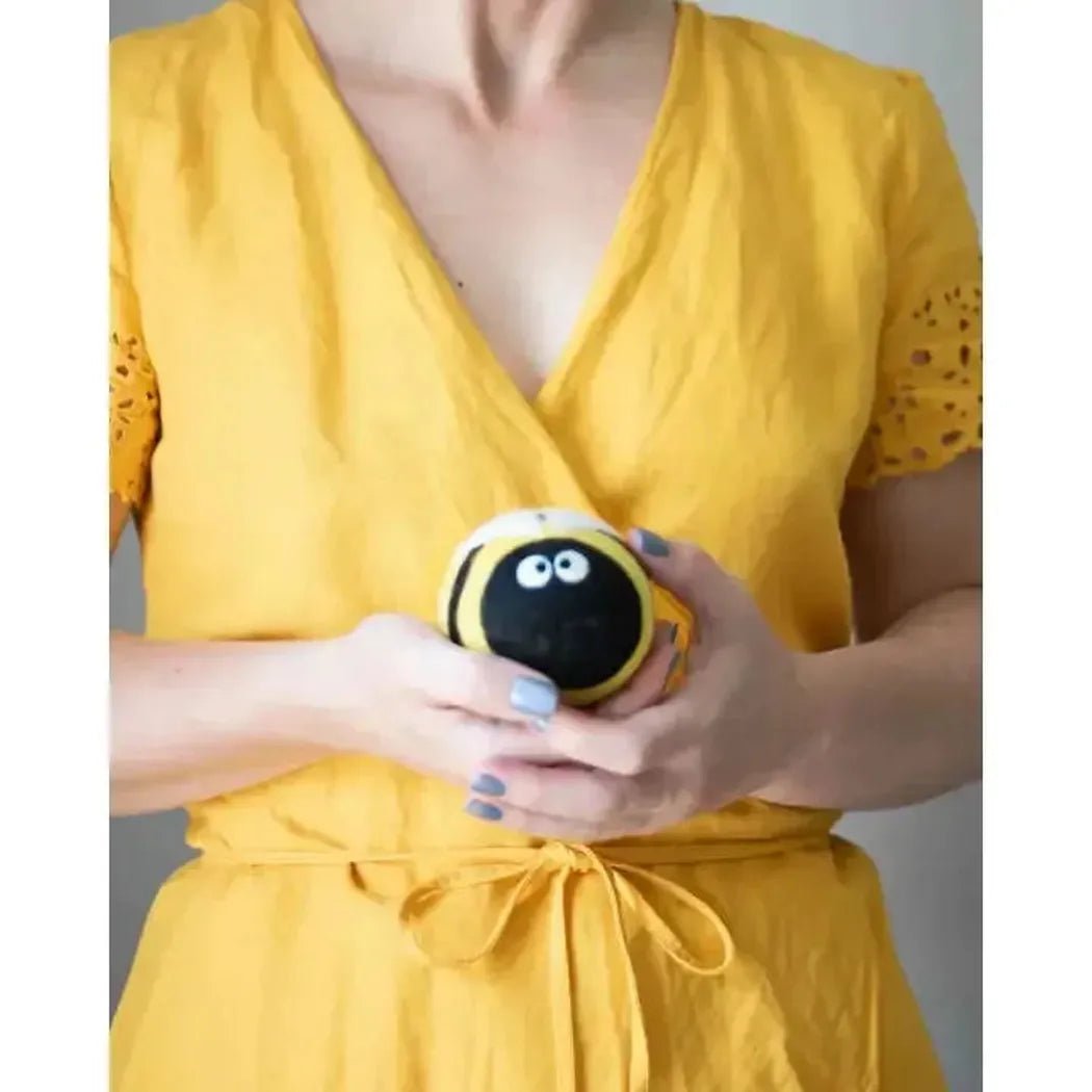 A woman in a yellow dress holds the Friendsheep Bee Trio Eco Wool Dryer Balls against a plain background.