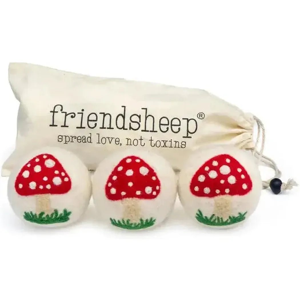 Three white felt mushroom balls with red caps and green grass bases sit in front of a cream drawstring bag labeled "friendsheep spread love, not toxins.