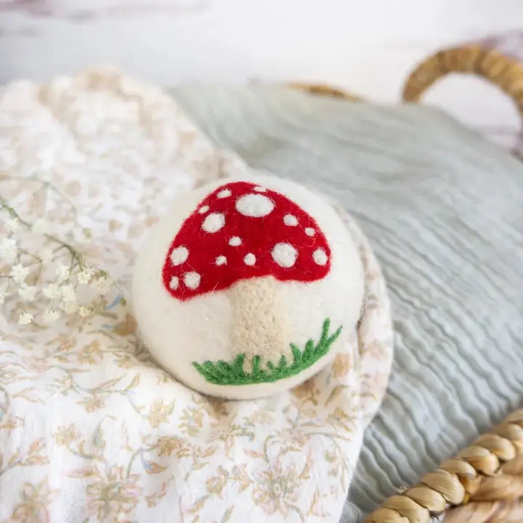 A close-up of the Friendsheep White Mushroom Trio with a red cap and white spots, sitting on a floral-patterned cloth.