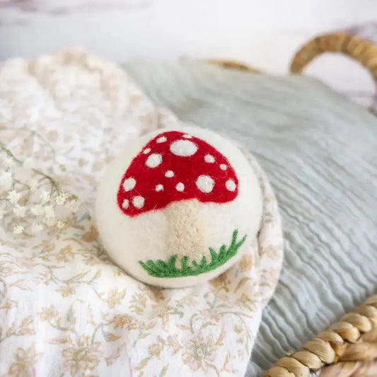 A close-up of the Friendsheep White Mushroom Trio with a red cap and white spots, sitting on a floral-patterned cloth.