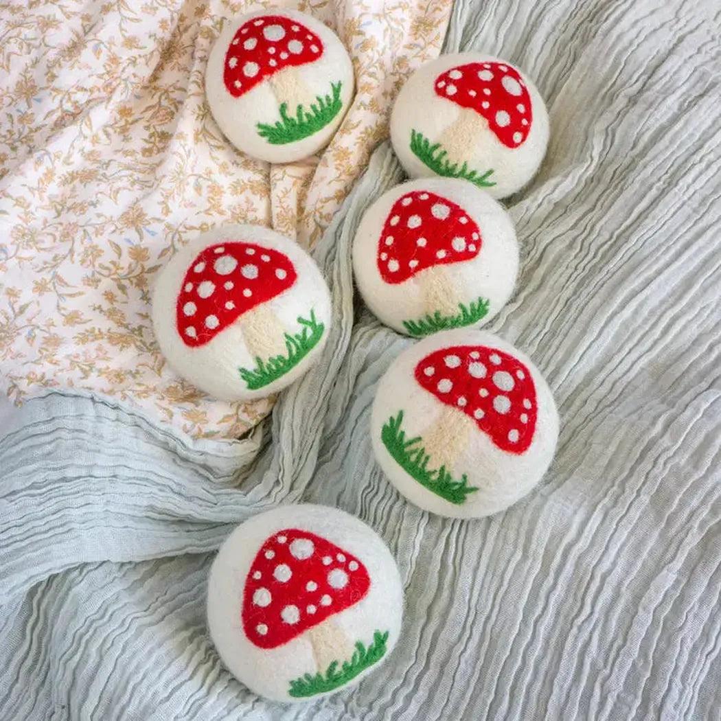 Six white wool balls with red mushroom tops and green grass sit on a floral and gray fabric background.