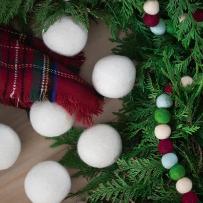 A top-down view of Friendsheep White Trio Eco Wool Dryer Balls scattered among green foliage and a red plaid fabric.
