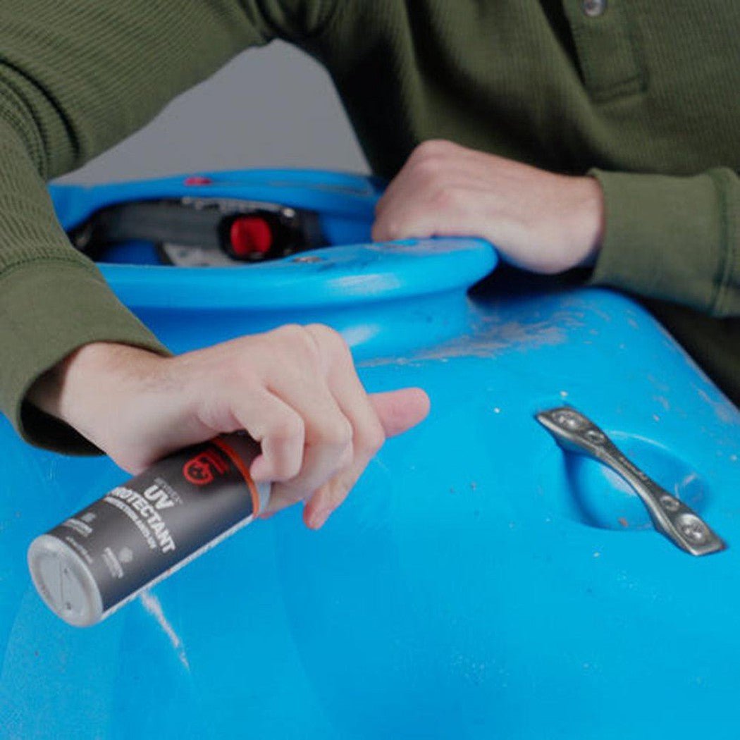 A person holds the Gear Aid Revivex UV Protectant spray can over a blue camping container with a metal handle.