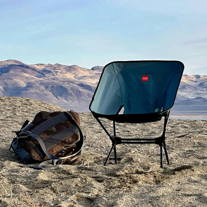 A side view of the Grand Trunk Caddis HD Chair in Storm Blue on a rocky desert landscape with mountains in the background.