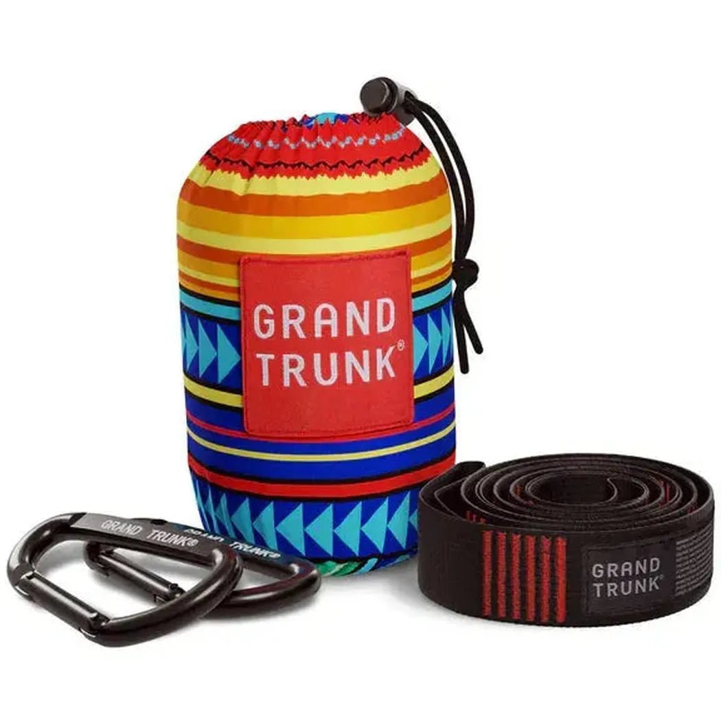 A colorful Grand Trunk bag with black carabiners and a black suspension strap with red stripes, all on a white background.