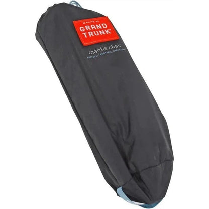 A black Grand Trunk Mantis chair in its carry bag, showing the red brand label and a light blue strap at the bottom.