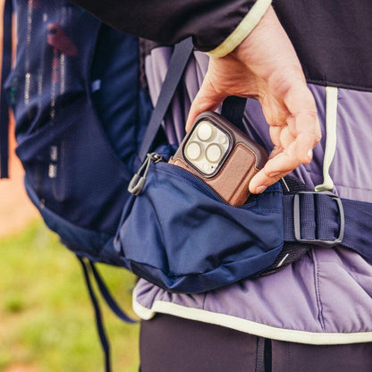 A person wearing a Coral Blue Gregory Amber 68 backpack reaches into a front pocket to grab a phone.