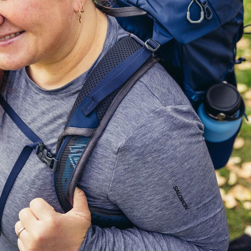 A woman wears the Gregory Jade 28 LT Plus backpack in Midnight Navy, showing the shoulder strap and a water bottle attached.