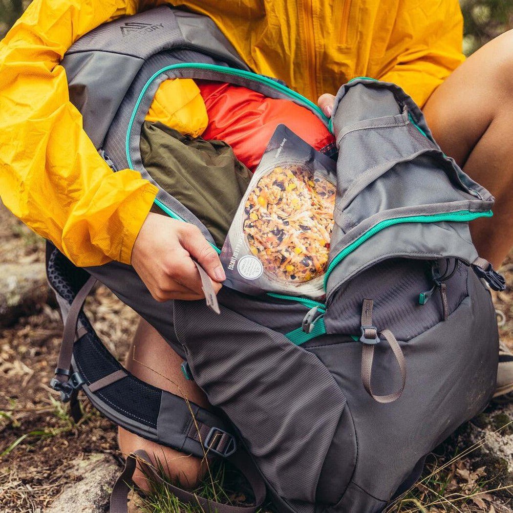 A person in a yellow jacket sits on the ground with the Gregory Jade 43 backpack open, showing its interior and a bag of food inside.