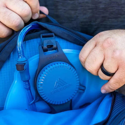 A close-up of the Gregory Miko 20 Plus Volt Blue daypack showing the hydration reservoir and a person's hands holding the zipper.