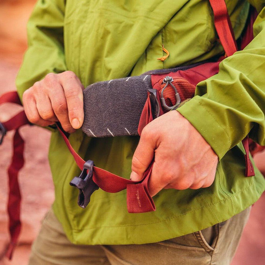 A person in Ferrous Orange Gregory Paragon 58 adjusts the waist belt with a charcoal/gray pocket visible.