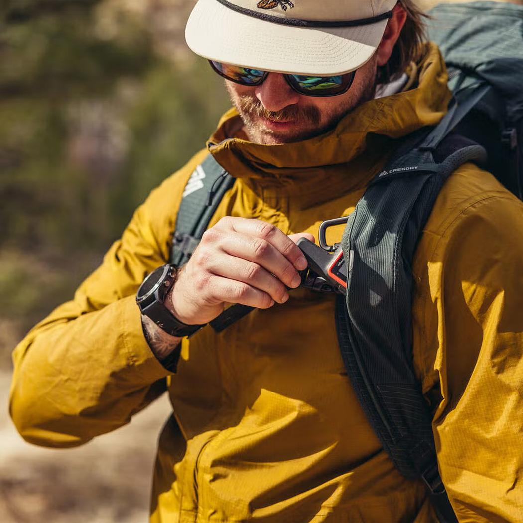 A man in a yellow jacket adjusts the Gregory Paragon 70 backpack in a natural outdoor setting.