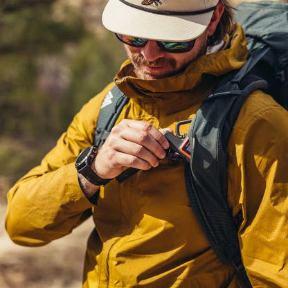 A man in a yellow jacket adjusts the Gregory Paragon 70 backpack in a natural outdoor setting.