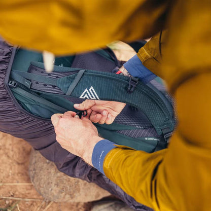 A person in a yellow jacket adjusts the straps of the Gregory Paragon 70 backpack on a rocky ground.