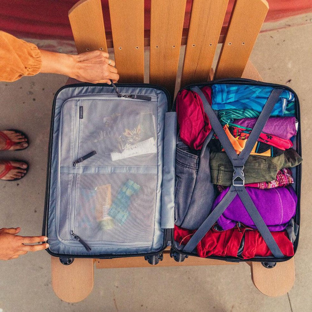 A top-down view of the Gregory Quadro Hardcase 22 in Total Black, showing the packed interior with colorful clothes and the mesh pocket on the left.
