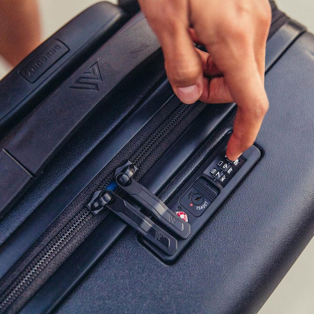 A hand adjusts the combination lock on the Gregory Quadro Hardcase 22 travel luggage in Total Black.
