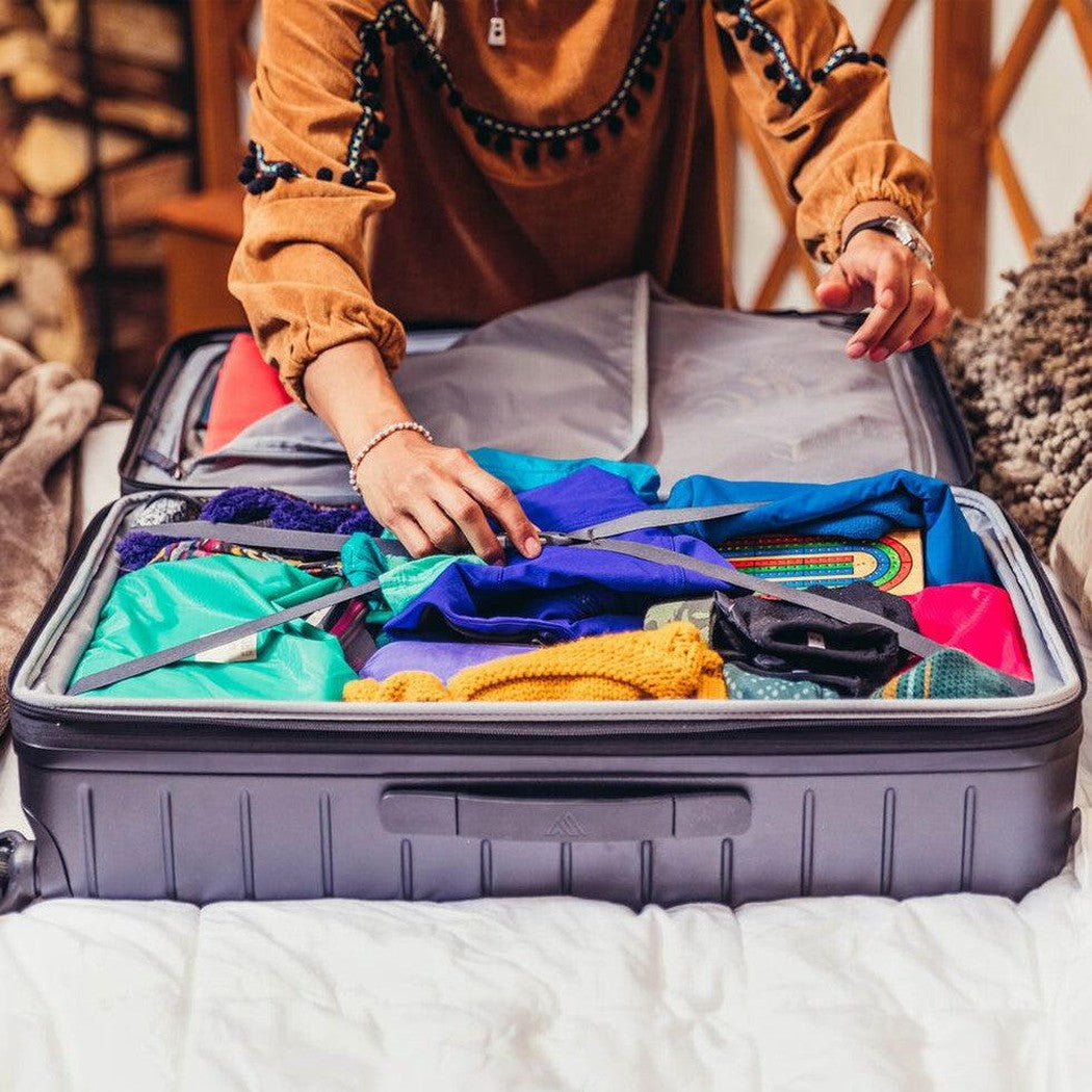 A person packs colorful clothes into a Total Black Gregory Quadro Hardcase 28 suitcase on a bed.