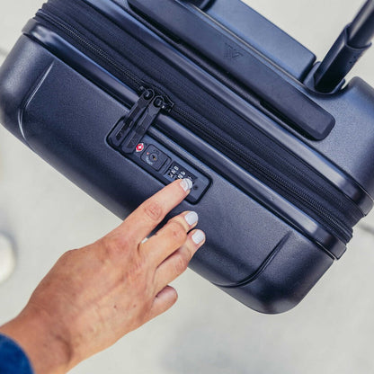 A hand presses the lock on the Gregory Quadro Pro 28 travel luggage in Optic Black, shown from a top-down angle.
