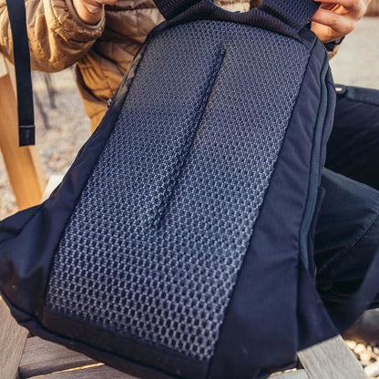 A close-up of the Gregory Rhune 22 daypack in Cabon Black, showing its mesh back panel and a person holding it outdoors.
