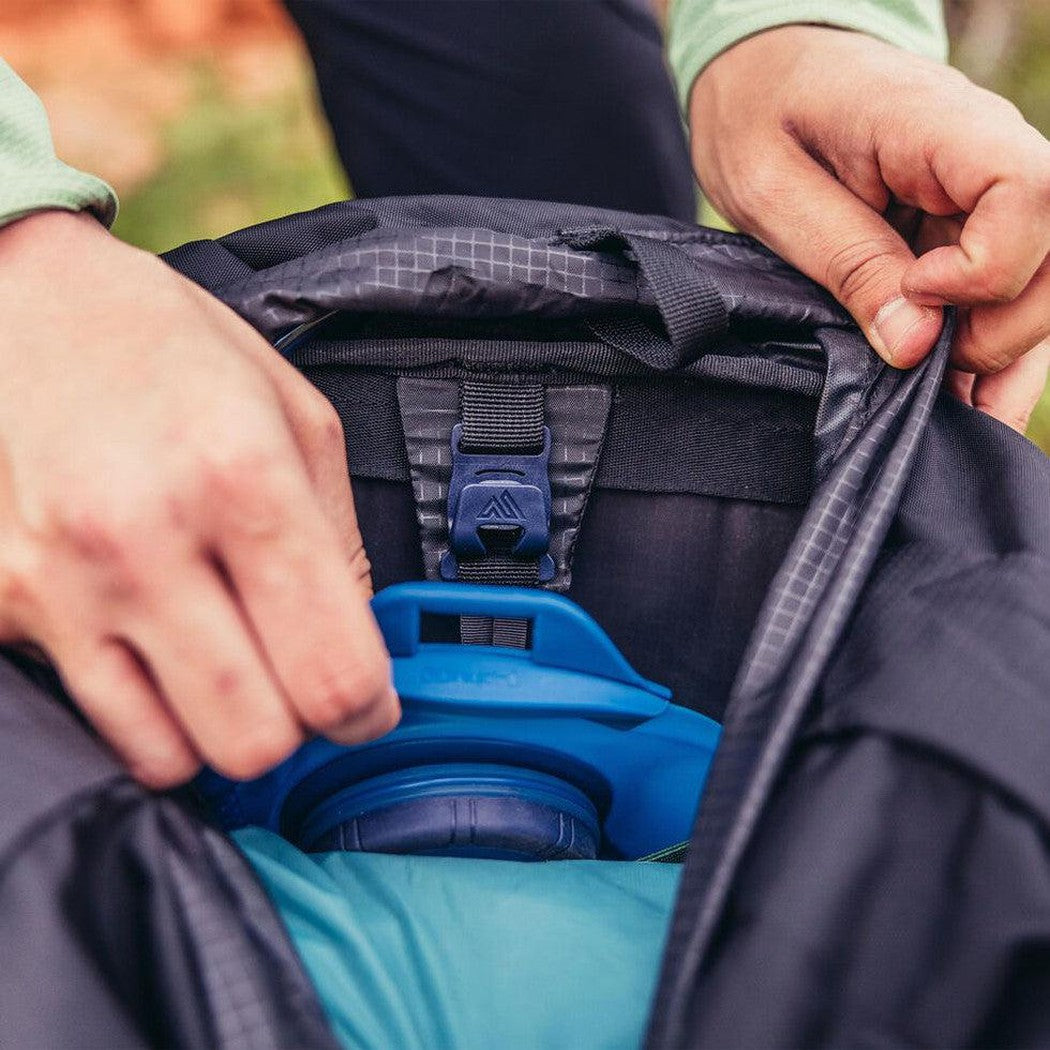 A person adjusts the Gregory Stout 70 backpack's top lid, revealing the blue hydration reservoir inside.