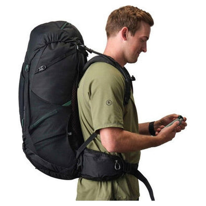 Side view of the Gregory Stout 70 Forest Black backpack on a model wearing it, showing the large main compartment and hip belt against a white background.