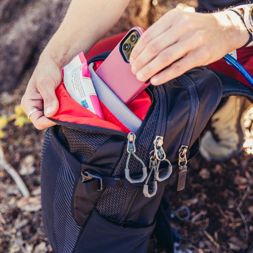 A person reaches into the Antigua Green Gregory Sula 8 H20 daypack, showing its red interior and mesh pockets.