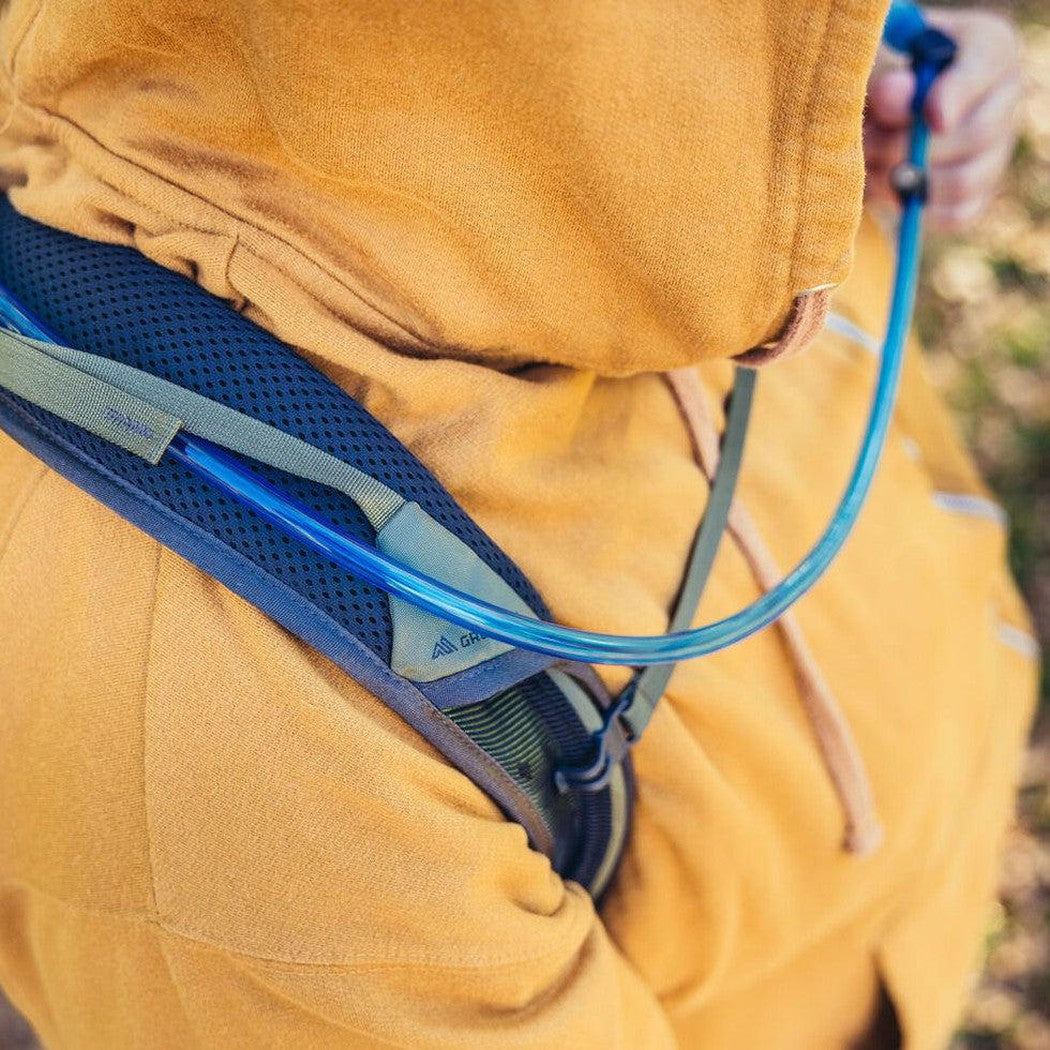 A person in a Forage Green hoodie wears the Gregory Zulu 28 LT Plus backpack with a blue hydration tube visible.
